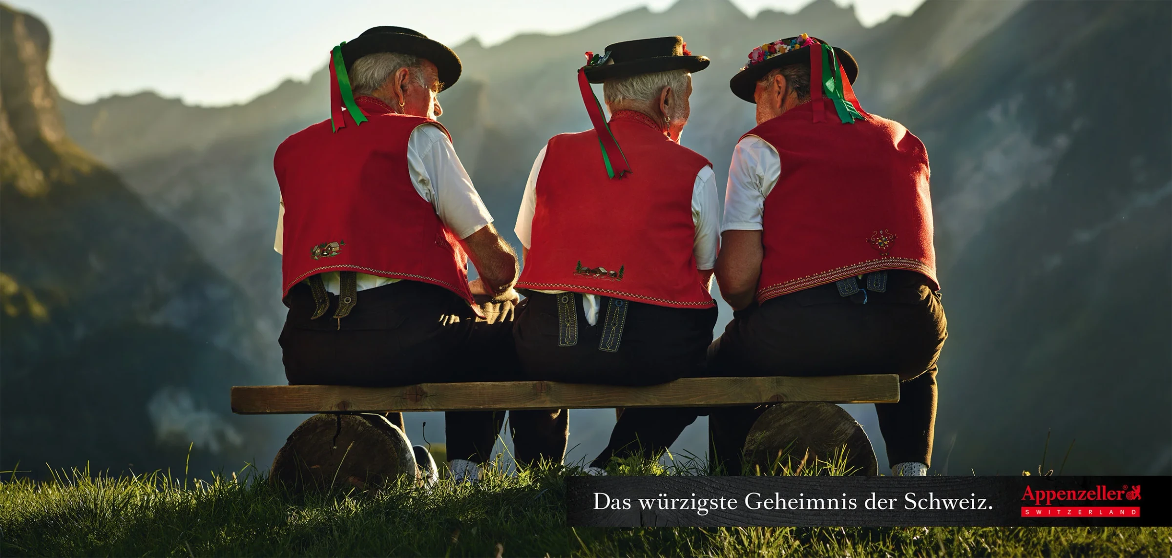 Affiche Appenzeller : trois hommes en costume traditionnel, de dos face aux montagnes.