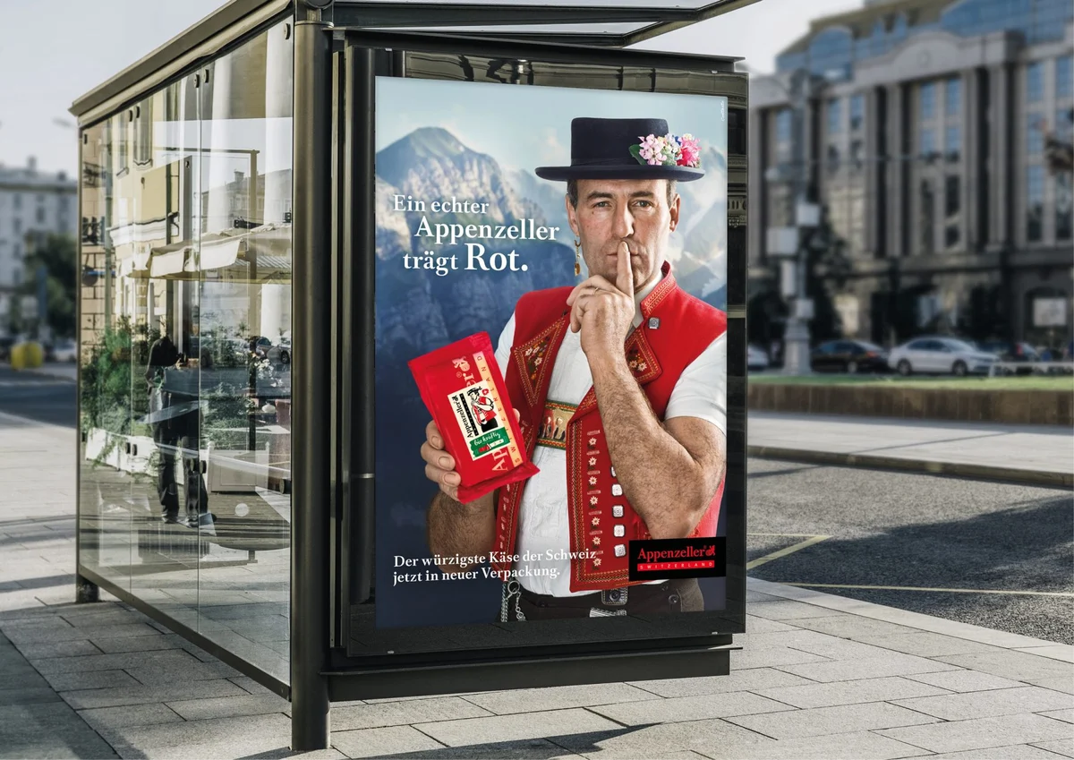Affiche Appenzeller en abribus : personnage en gilet rouge, doigt sur les lèvres.