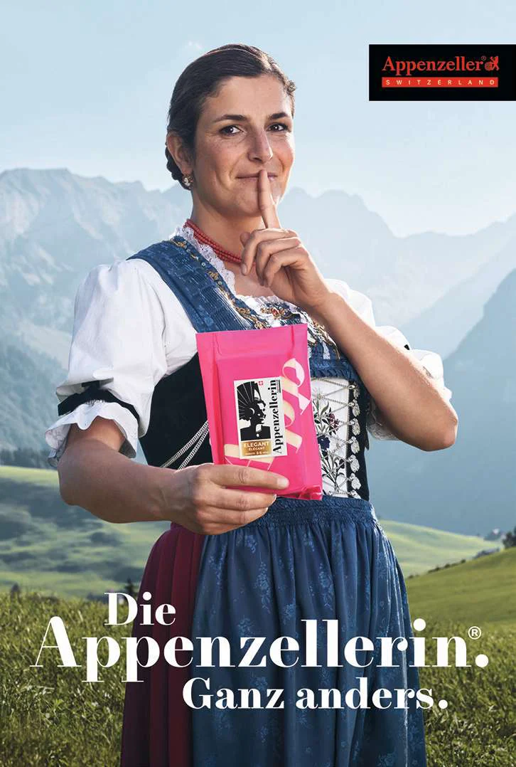 Affiche Appenzellerin « Ganz anders » avec une femme en costume traditionnel devant les montagnes.