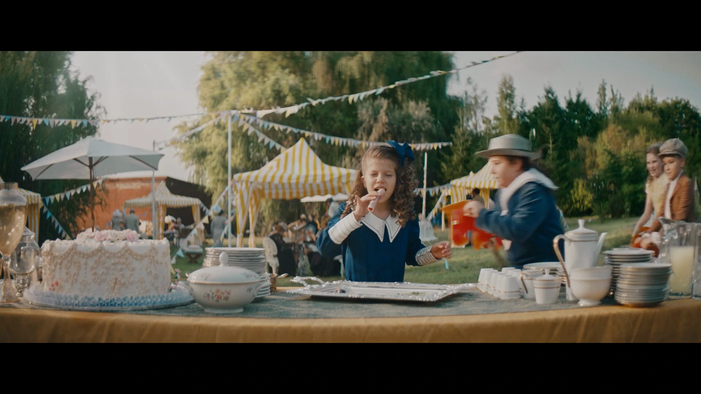 Film anniversaire Bell : une enfant goûte un aliment à un buffet en plein air.