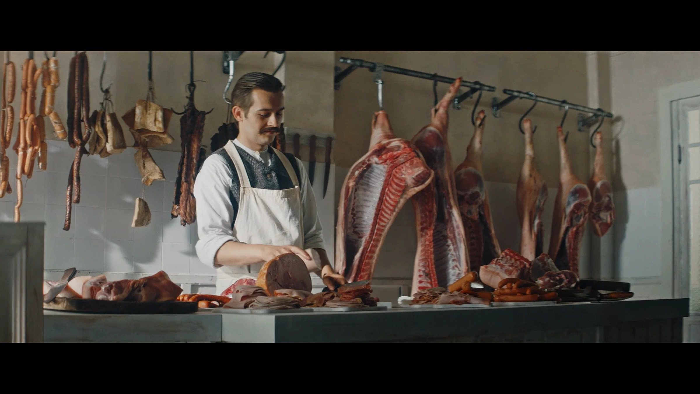 Film anniversaire Bell : boucher derrière son comptoir dans une boutique ancienne.