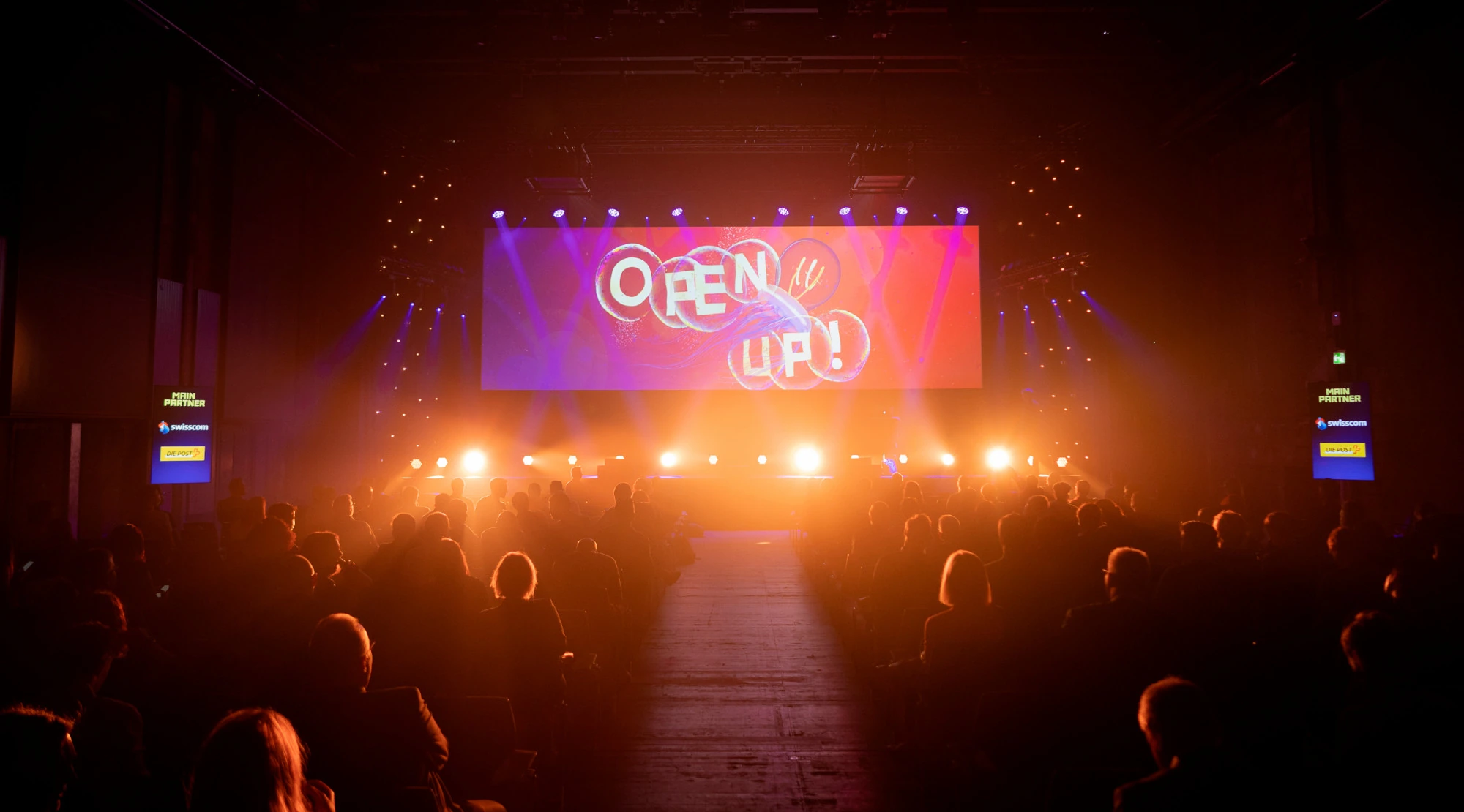 Scène éclairée en orange avec le visuel « Open Up! » du Digital Festival.